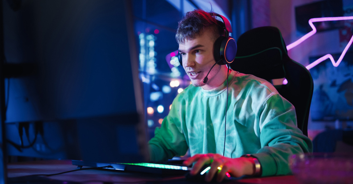 Young man gaming on a desktop computer with headphones in a neon-lit room, featured in a Yomojo article about upcoming home internet plans in Australia.